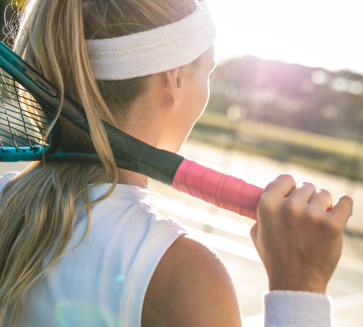 Rear view of young blond caucasian female tennis player with racket around neck at court. unaltered, sport, competition and tennis game concept.